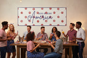 Patriotic “God Bless America” matte banner with red polka dot background hanging above a party table, 96x36 inches.