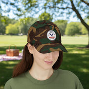Girl wearing all camouflage classic ball cap with a circular emblem featuring an eagle and text , along with the American flag on the side in front of a picnic.