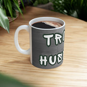'Trophy Husband' Mug side view on a wooden table with coffee.