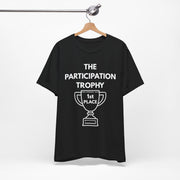 Black t-shirt with white text and white graphic on a hanger saying 'The Participation Trophy - 1st Place'