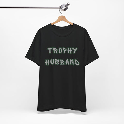 Black t-shirt with 'Trophy Husband' text on a hanger against a white background
