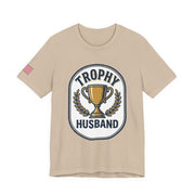 Beige t-shirt with 'Trophy Husband' graphic on a white background