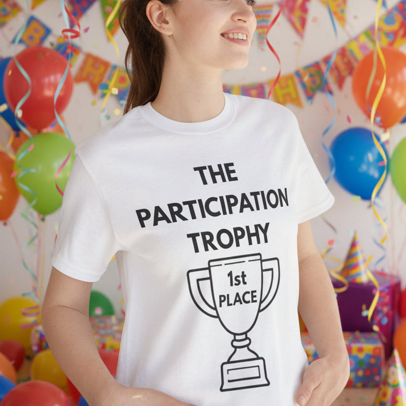 Female wearing a white t-shirt with 'The Participation Trophy' design, standing at a kids party.