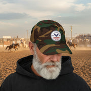 Man wearing camouflage classic ball cap with a circular emblem featuring an eagle and text , along with the American flag on the side on a white background.