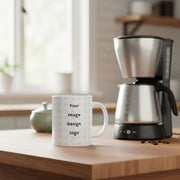 Customizable white mug with "your image or design" placeholder on a kitchen table next to a coffee maker. 