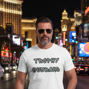 Man wearing a white t-shirt with 'Trophy Husband' text walking on street in vegas. 
