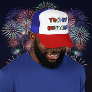 Man wearing a red white and blue cap with 'Trophy Husband' in red white and blue text, standing in front of fireworks.