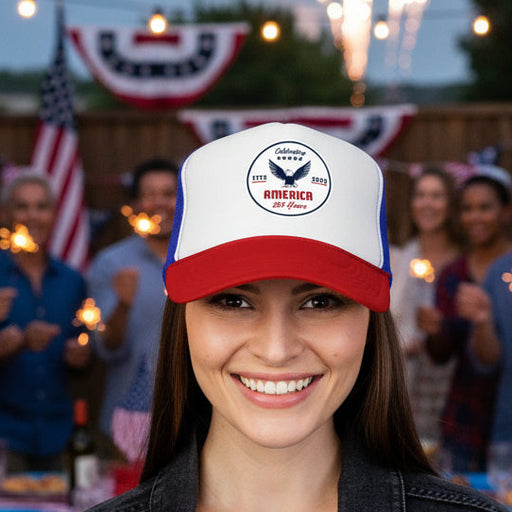 Red white and blue trucker hat with 'Celebrating America for 250 Years' design displayed on female in front of party. 