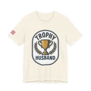Natural color t-shirt with 'Trophy Husband' graphic design on a white background