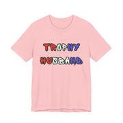 Pink t-shirt with 'Trophy Husband' in red white and blue text on a white background