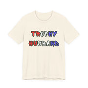 Beige t-shirt with 'Trophy Husband' in red white and blue text on a white background
