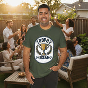 Man wearing a green t-shirt with 'Trophy Husband' graphic at a backyard party. 