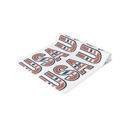 Table runner rolled up with 'USA' in red white and blue repeated on a white background. 