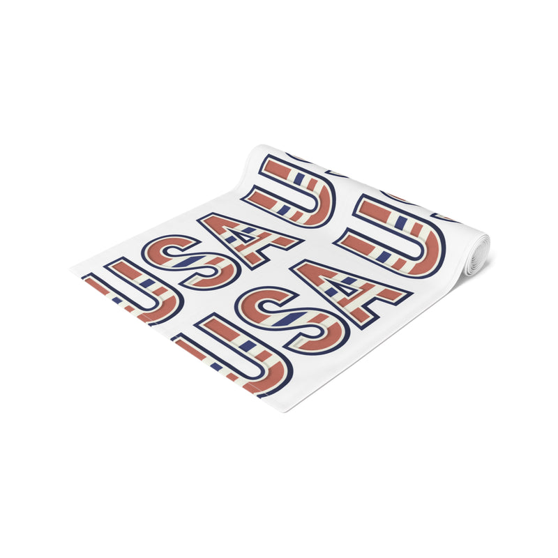 Table runner rolled up with 'USA' in red white and blue repeated on a white background. 