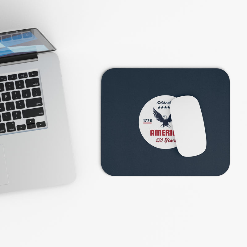 Navy blue mouse pad with a circular design featuring an eagle and text celebrating America's 250th anniversary with white mouse and a keyboard.
